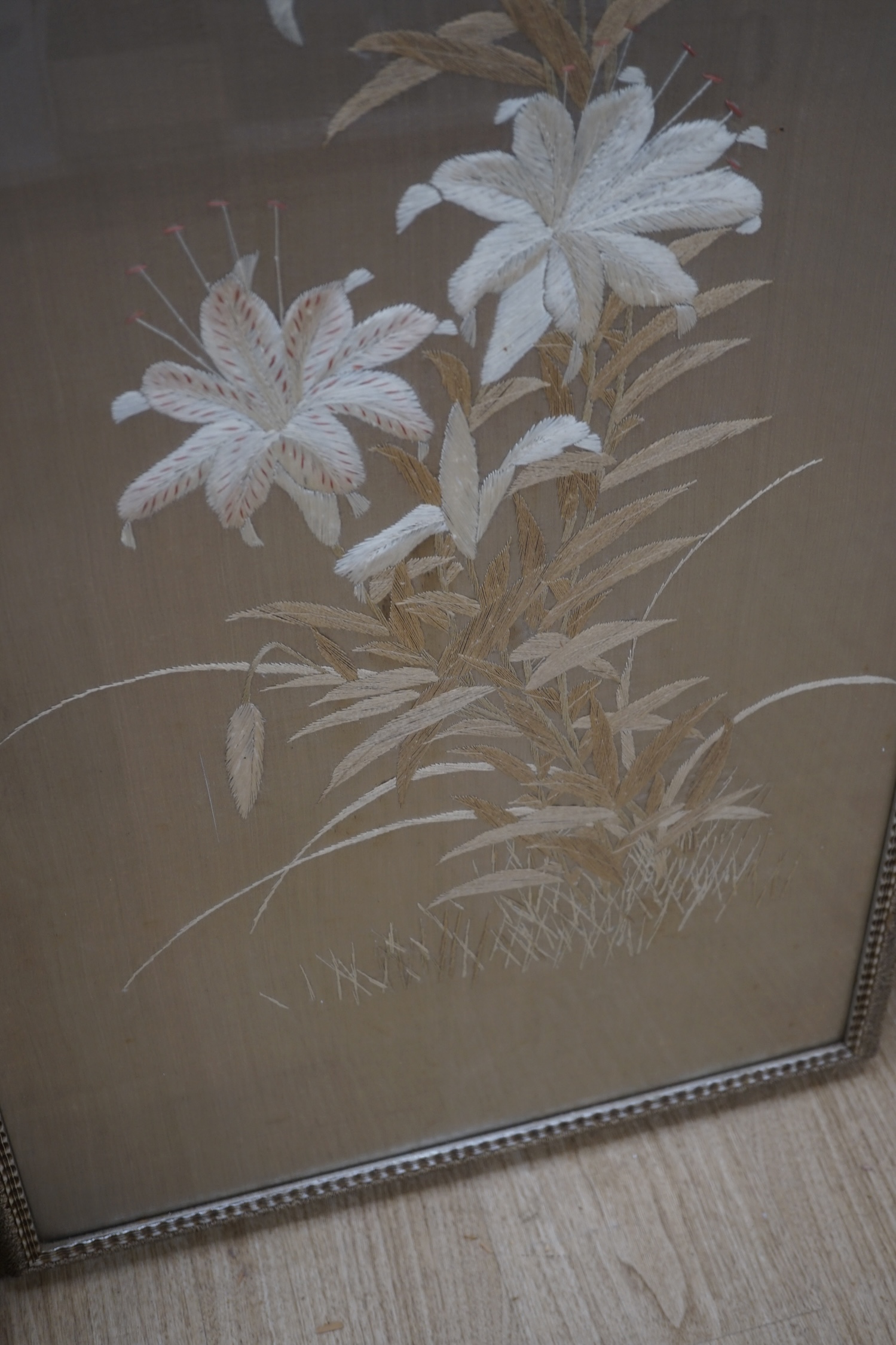 A 1900 to 1920’s Japanese silk embroidery of birds in flight and flowers on a grey background, 131cm high, 52cm wide, together with a Japanese silk and metallic thread still life embroidery on black background, with couc